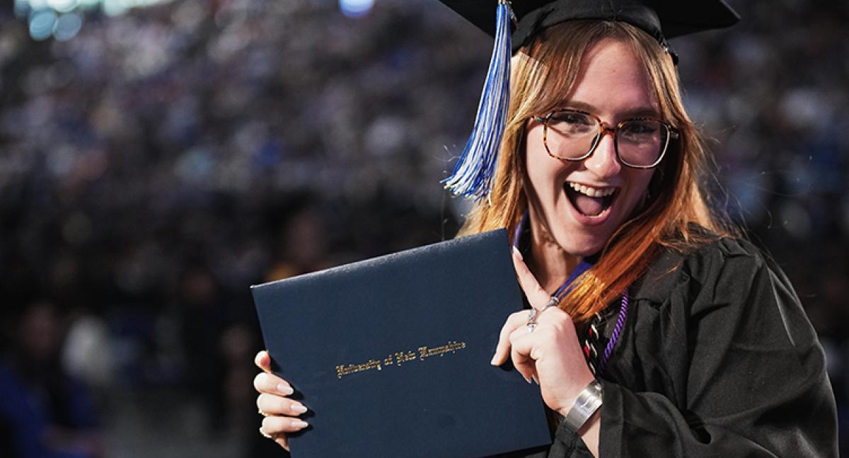 A female graduate smiles while displaying her diploma after walking across the stage