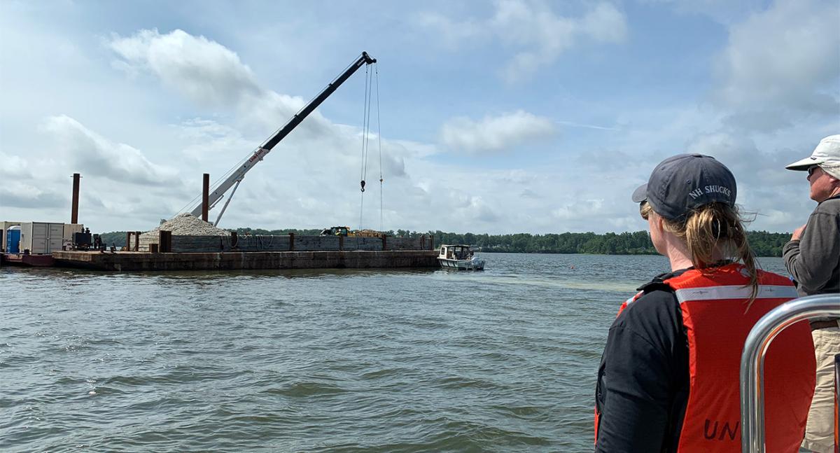 Laura Brown (left), owner of Fox Point Oysters, and Ray Grizzle, a UNH professor of biological sciences, watch as a crane operated by Riverside & Pickering Marine Contractors deposits oyster shells at the Nannie Island reef restoration site.