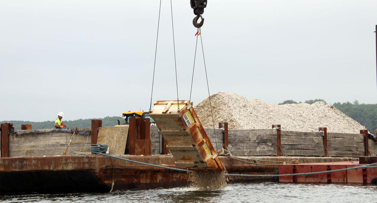 A crane drops seasoned shell into the water to establish substrate at the Nannie Island reef restoration site in Great Bay Estuary.