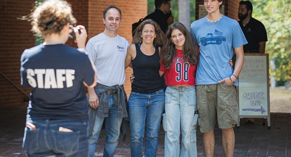 A UNH student takes a photo of a family of four outside of a dorm room on move-in day