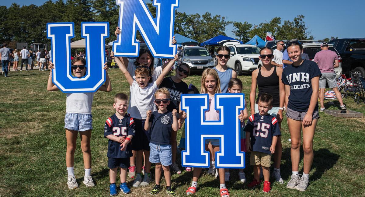 A group of young children gather, holding up the letters U, N and H