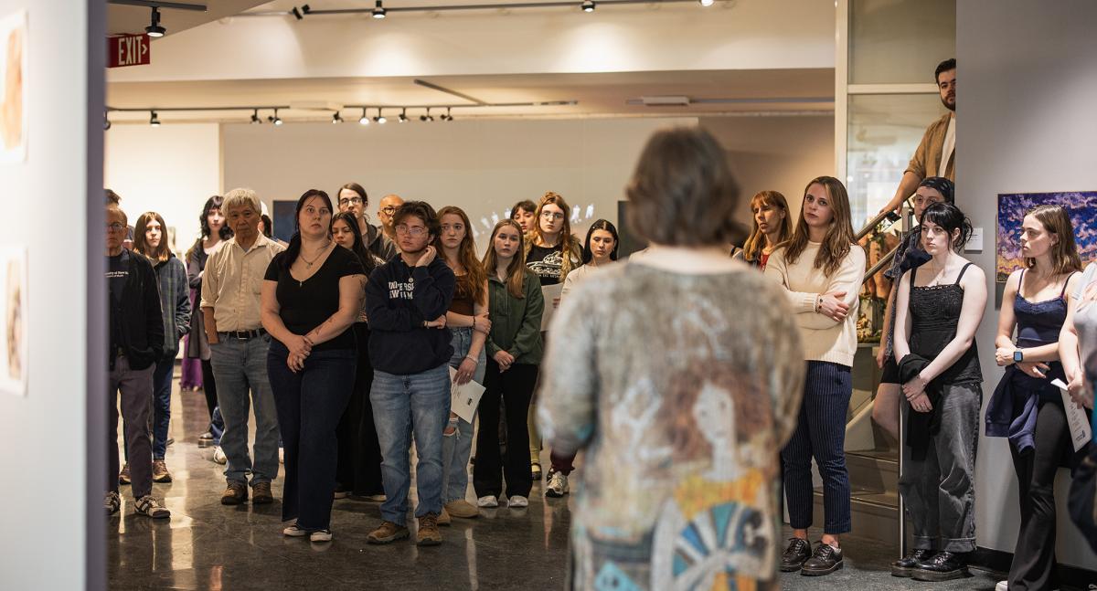 A group of onlookers listens to a presentation in an art gallery