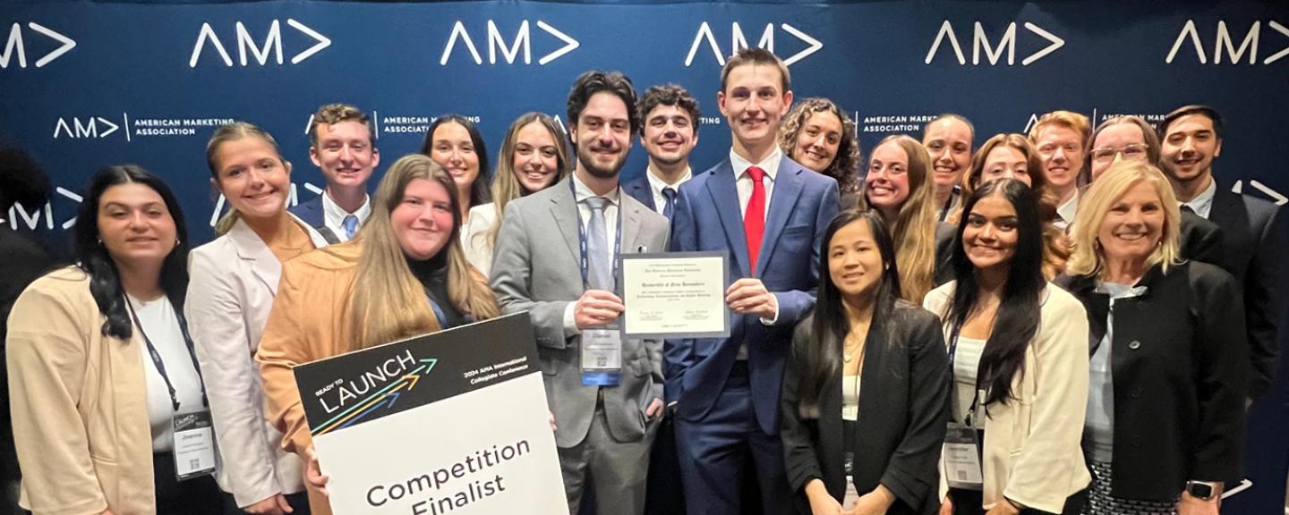 A large group of UNH Marketing majors gathers for a photo opportunity at the American Marketing Association's International Collegiate Competition. One student holds a sign that reads, "Competition finalist."
