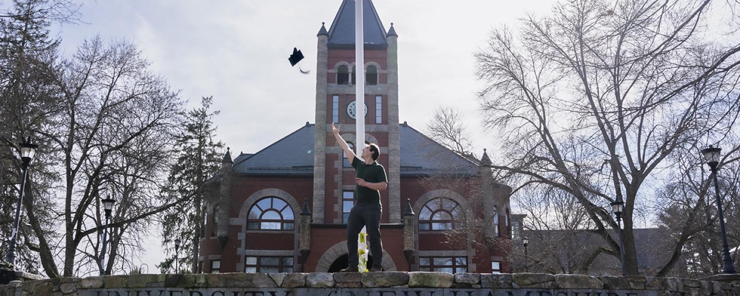 Diego Smith tosses his graduation cap into the air in celebration in front of thompson hall.