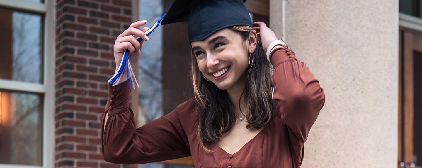 Hannah Donahue adjusts her graduation cap while sitting on steps at UNH campus.
