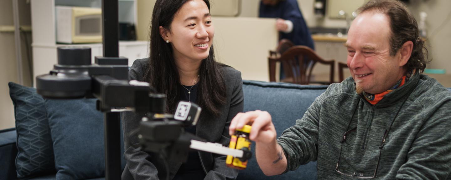 Two people, a young woman and an older man, sit on a couch with a robot in front of them