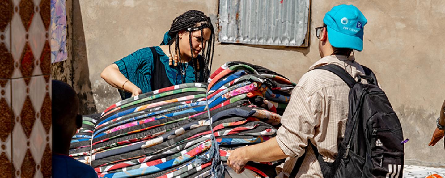 A man and a woman carry a bundle of colorful mats  
