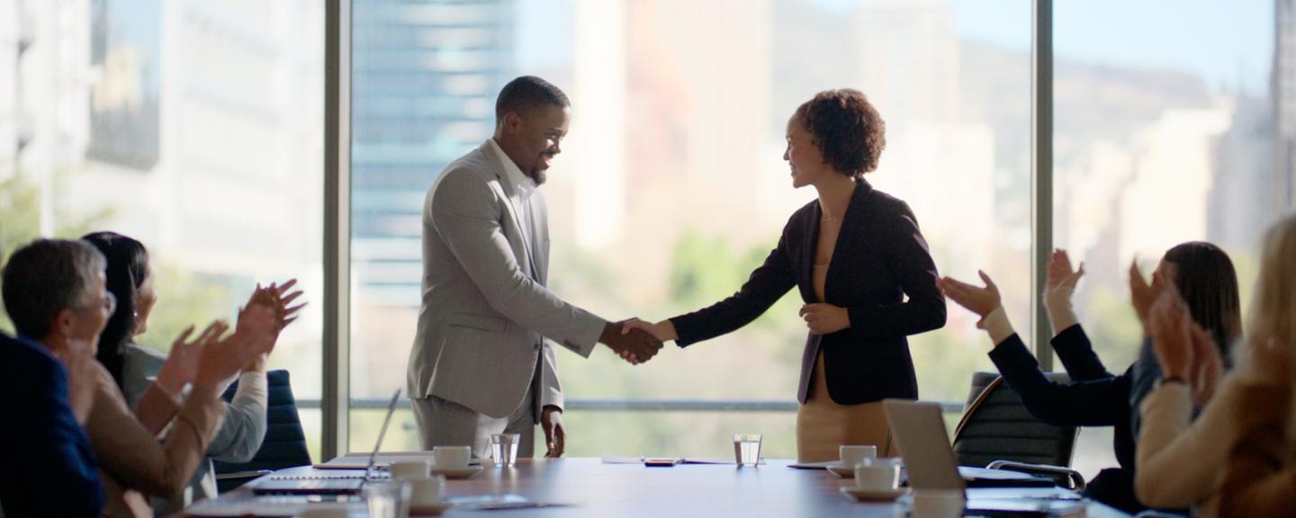A man and woman shaking hands in front of a table of people