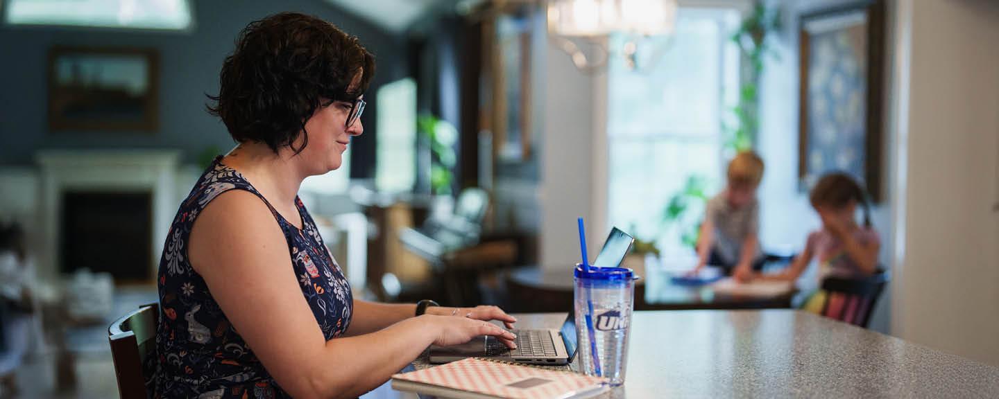 Woman on laptop in her kitchen and kids in the background 