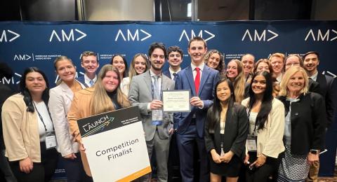 A large group of UNH Marketing majors gathers for a photo opportunity at the American Marketing Association's International Collegiate Competition. One student holds a sign that reads, "Competition finalist."
