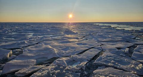 A frozen body of water with the sun low on the horizon