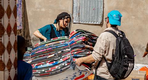 A man and a woman carry a bundle of colorful mats  