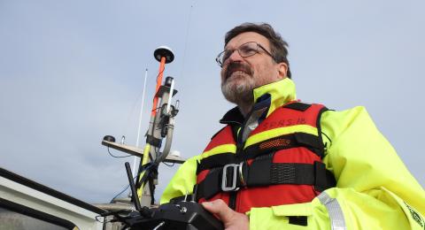 Brian Calder wears a life jacket and holds a remote controller while aboard a boat. 