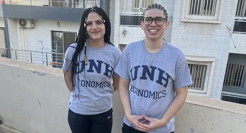 A woman and a man, both wearing UNH economics T-shirts, pose for a photo together