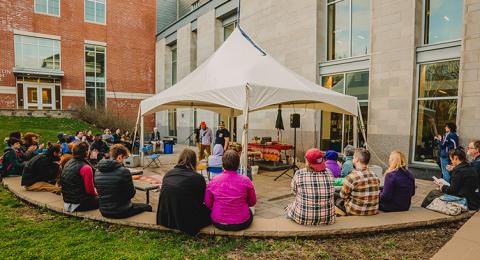 A crowd sits in a semi circle around a small stage with two performers