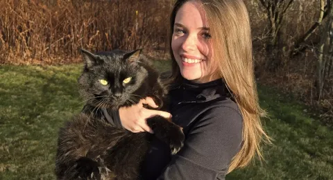 UNH undergraduate Kaley Dupont poses outside with a black cat