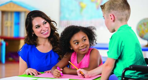 photo of woman working with two children at a table in a classroom