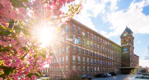 Photo of brick building on a sunny spring day, with pink flowers in front. 