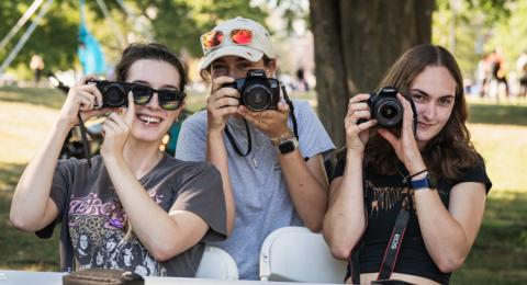 Three female students hold up cameras while smiling