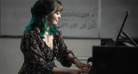 A woman sits at a piano bench and plays, in front of a white board with musical notes on it