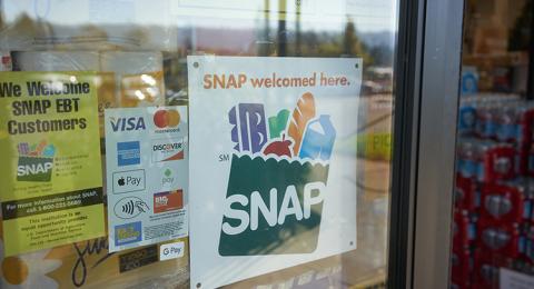 A window of a retail store displays a SNAP welcomed here sign