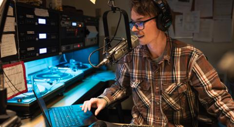 A male student wearing glasses mans the DJ booth in the WUNH studio