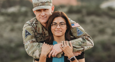 A man in military fatigues wraps his arms around the shoulders of a woman in a teal shirt and black sweater