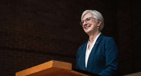 UNH President Elizabeth Chilton in a blue blazer stands at a podium and smiles to the crowd