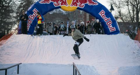 A snowboarder goes airborne off a ramp in an attempt to land on a rail