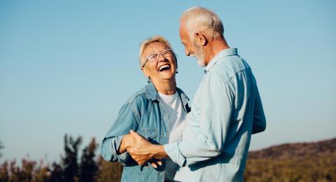 Stock image of an older couple laughing outdoors in the sunlight.