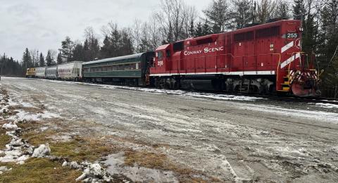 A locomotive pulling several passenger cars is shown on tracks.