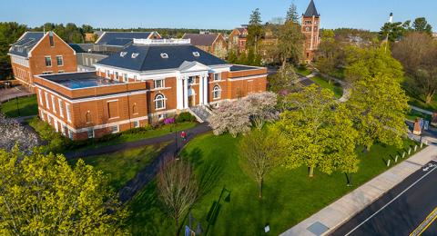 Aerial photo of brick academic buildings behind green trees in early spring