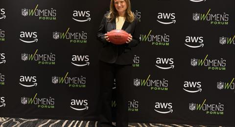 A woman in a black suit holds a football in front of her in front of a black backdrop