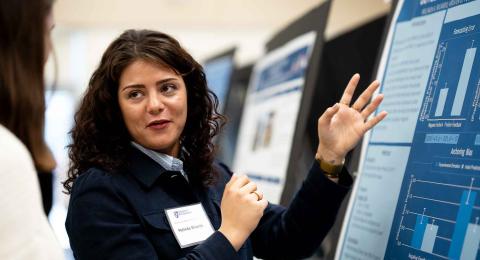 A woman looks back while speaking to a guest as she explains research on a poster in front of her