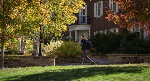 Image of a male UNH student walking on campus surrounded by bright fall foliage