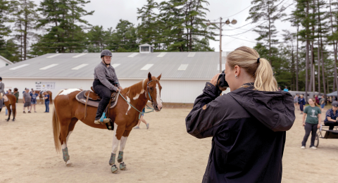 A woman takes a photo of an equestrian competition