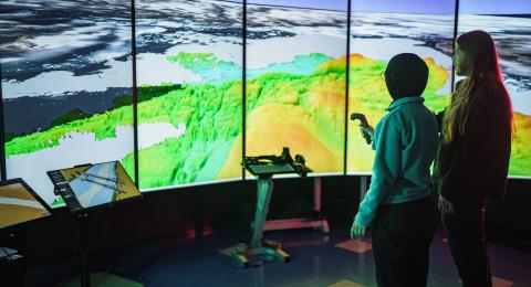 Two people stand in front of the large screen inside UNH's Data Visualization Research Lab at the Center for Coastal & Ocean Mapping