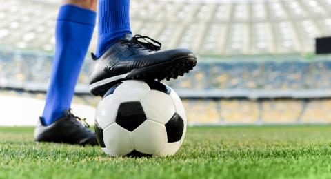 Soccer players holds ball with foot.