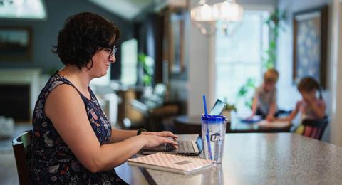Woman on laptop in her kitchen and kids in the background 