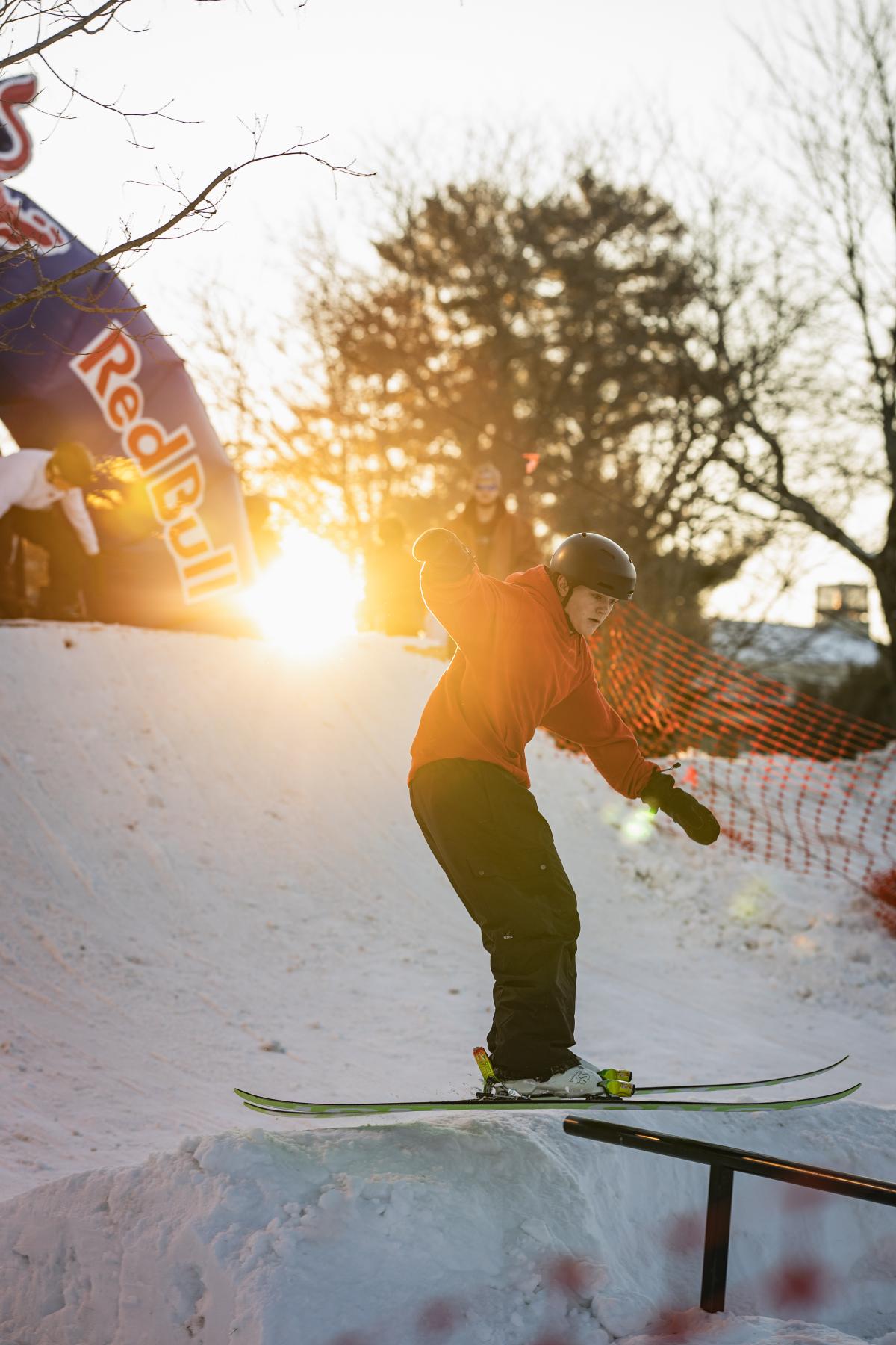 The sun glints in the background as a skier prepares to glide along a rail