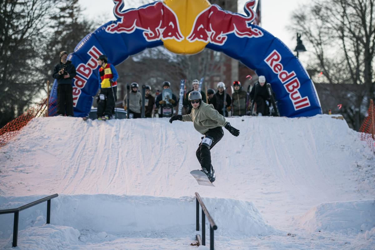 A snowboarder goes airborne off a ramp in an attempt to land on a rail