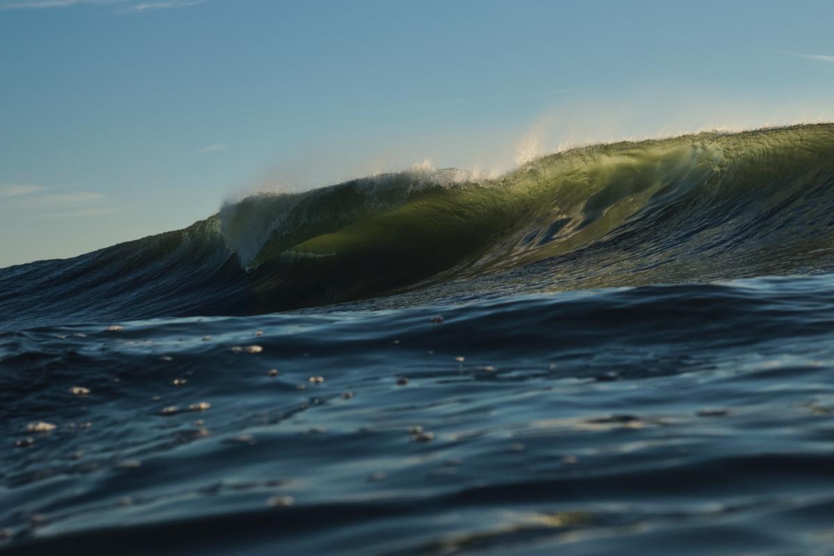 A wave glints in the sun as it prepares to crash