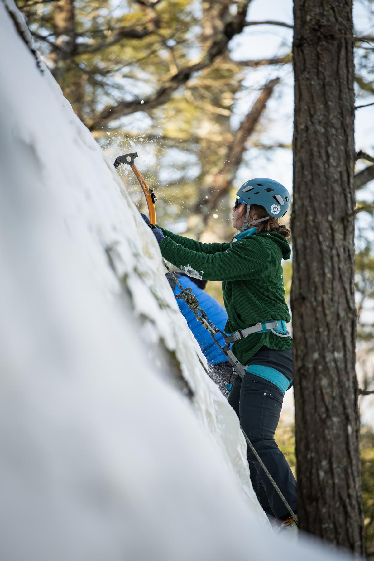 Chips of ice spray into the air as a woman climbs the side of an icy cliff face