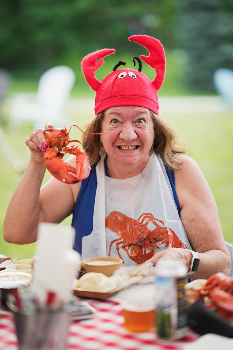 A woman in a lobster hat holds up a lobster at reunion