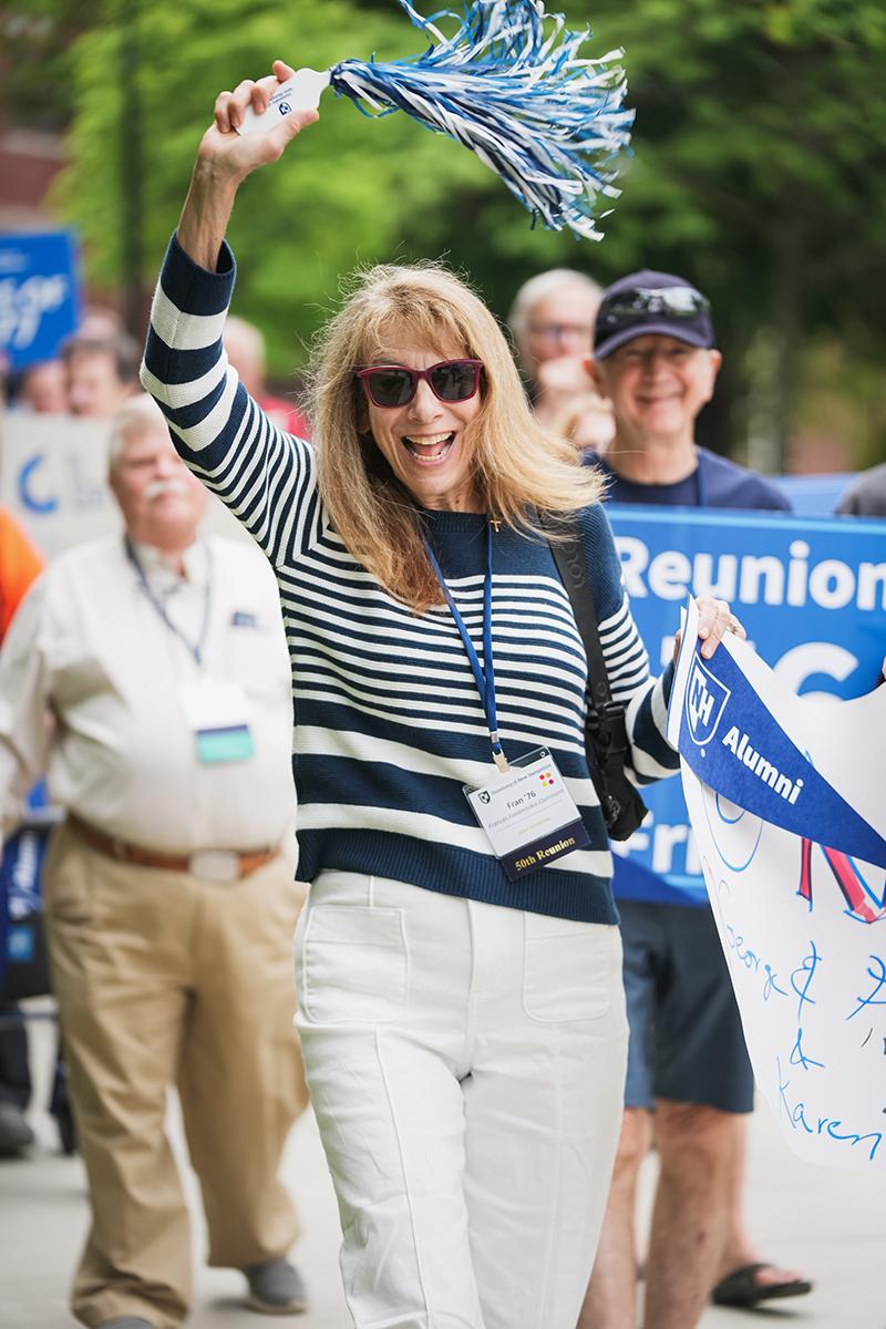 A woman waves a small pom pom while walking in the reunion parade