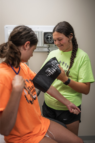 Female student putting blood pressure sleeve on another student