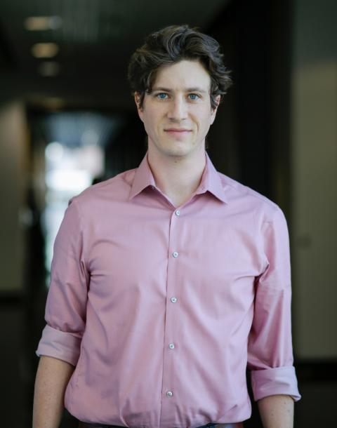 Male researcher wearing pink shirt stands in a hallway