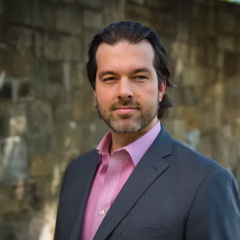 UNH alumni Jason Alme poses in front of stone wall