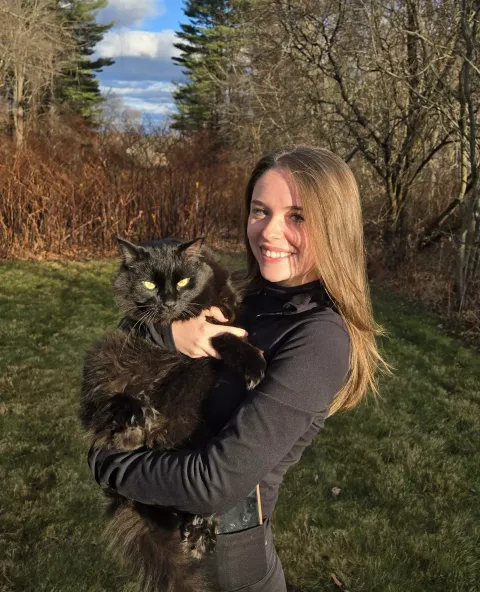 UNH undergraduate Kaley Dupont poses outside with a black cat