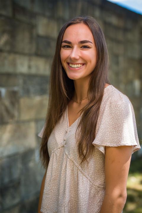 Master of Science in Nutrition student Kelli Street. Kelli has tanned white skin. She has brown hair that goes down to her chest. She wears a off-white shirt with a floral print.